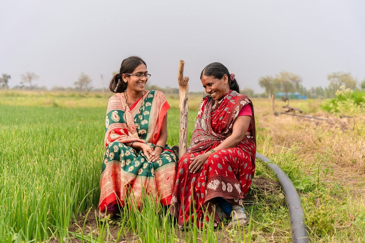 Two women sit and talk at the edge of a green field