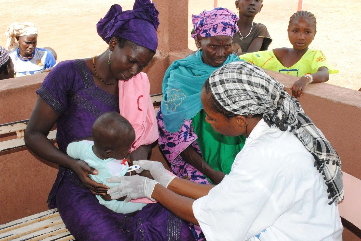 A community health worker checks a small child held by her mother during a health visit in Mali