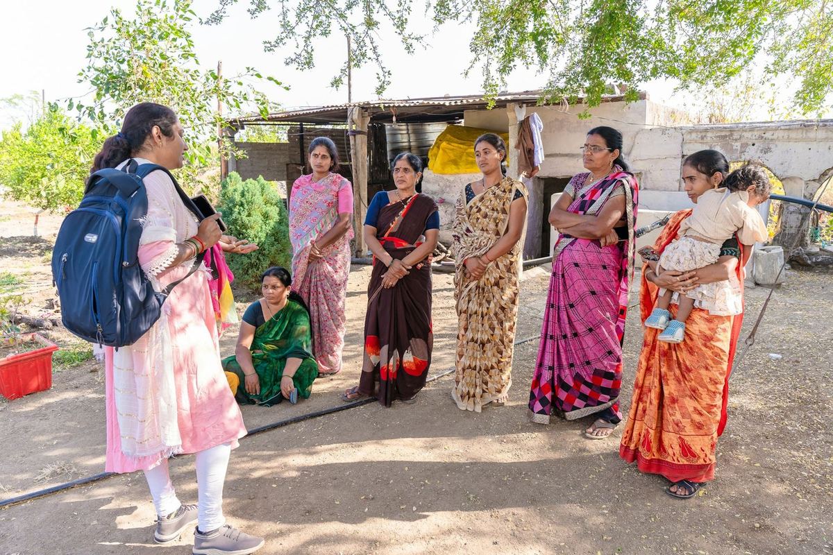 A fieldworker with a backpack talks with a group of women outside their homes in a village